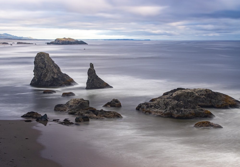 a beach with rocks in the water and a cloudy sky