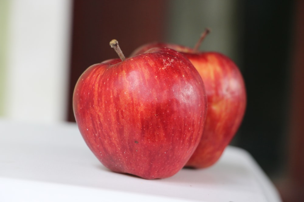 two red apples sitting on top of a white table