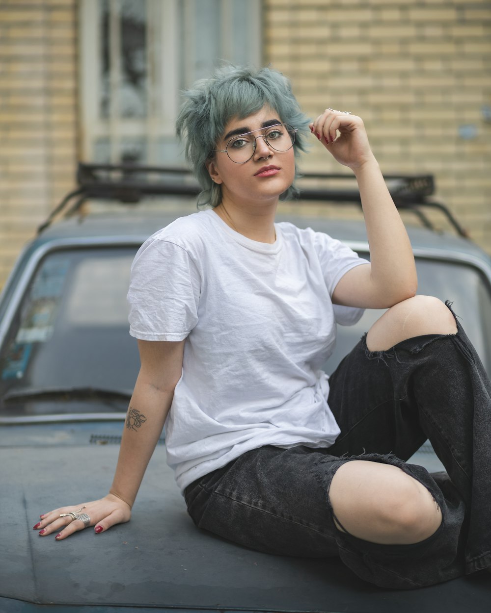 eine frau mit grünen haaren, die auf der motorhaube eines autos sitzt