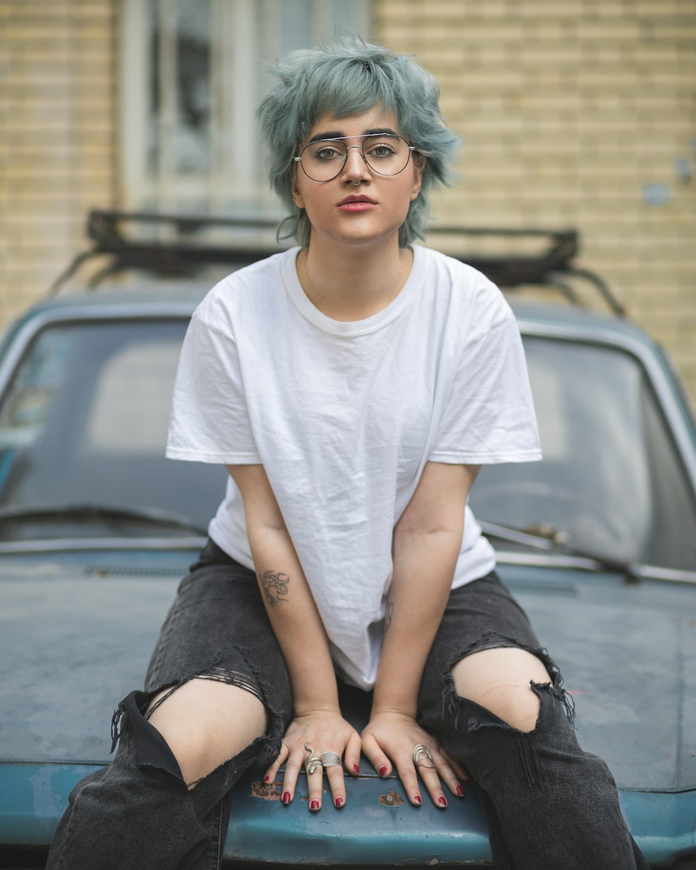 a woman with blue hair sitting on the hood of a car