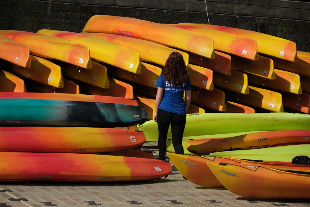 a woman standing next to a pile of kayaks