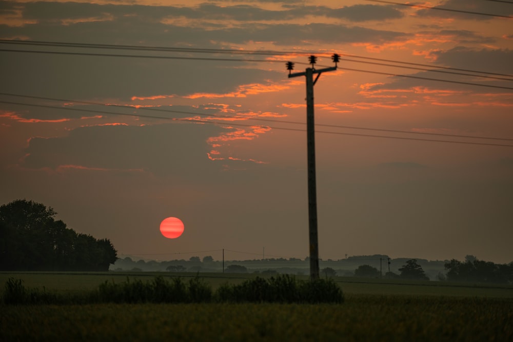 the sun is setting over a field with power lines