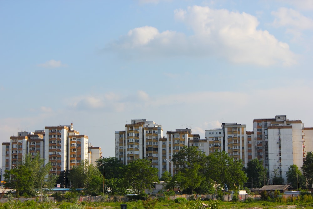 a group of tall buildings sitting next to a lush green field