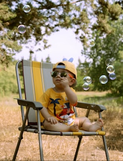 a little boy sitting in a lawn chair blowing bubbles