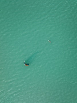 Dynamic drone footage capturing a kite surfer performing tricks over turquoise water.
