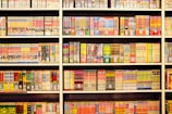 A bookshelf filled with numerous manga volumes organized neatly in rows. Each book is vividly colored, featuring different styles of artwork typical of Japanese manga. The spines display a variety of titles, characters, and symbols, creating a lively and engaging visual experience.