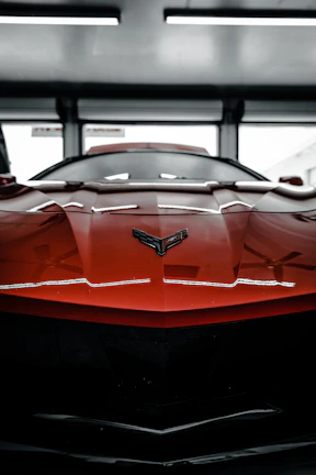 Close-up of a freshly painted red sports car hood gleaming under shop lights.