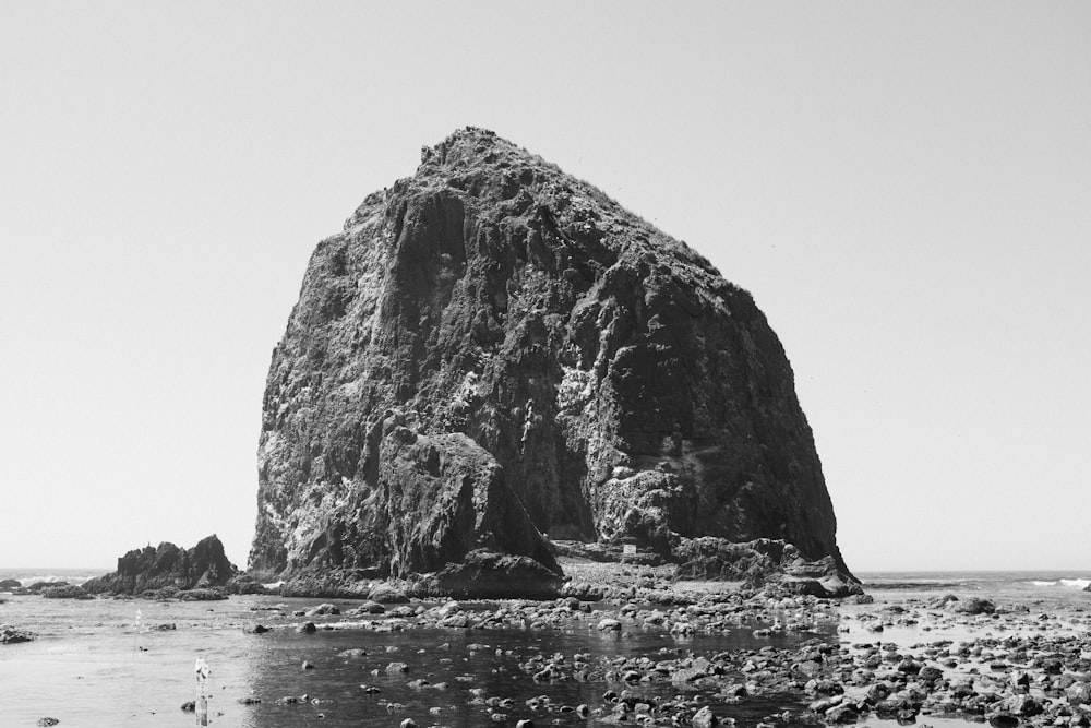 ein großer Felsen, der auf einem Strand neben dem Meer sitzt