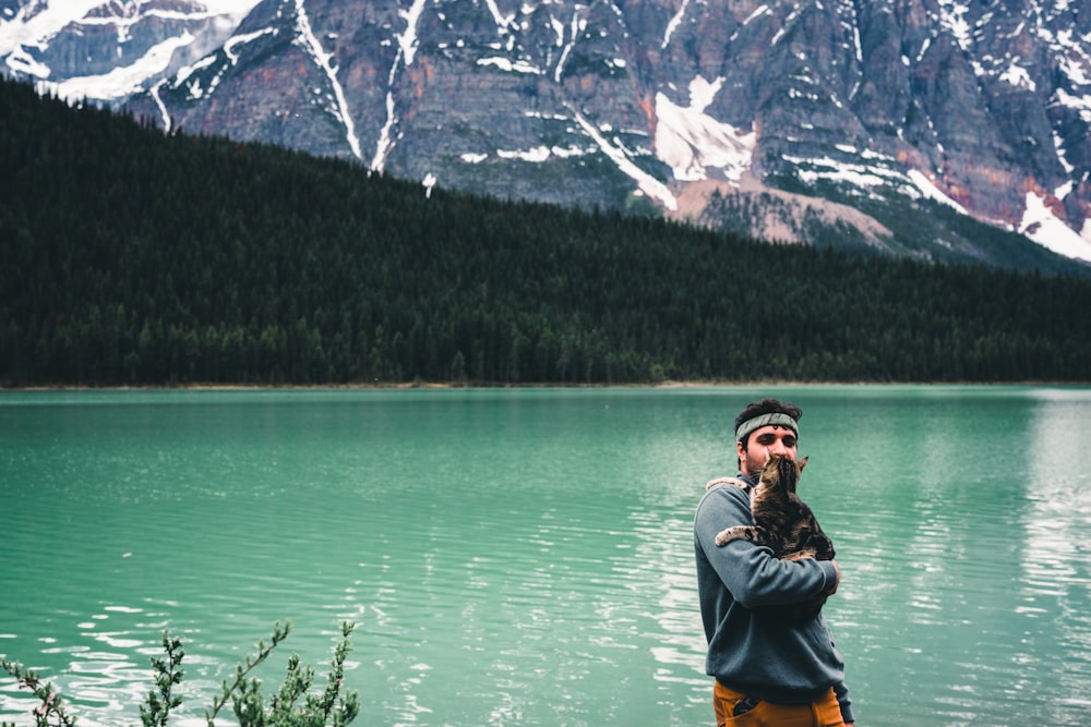 a man with a beard standing in front of a mountain lake