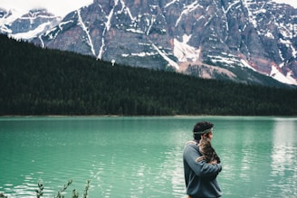 a man holding a cat standing next to a lake