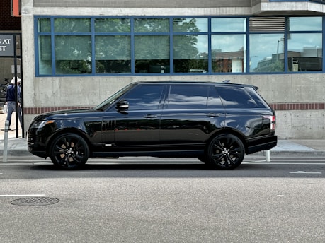 A glossy black SUV parked curbside with a chauffeur opening the door.
