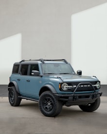 A rugged SUV with four doors and large tires, painted in a muted blue color. The vehicle features distinctive headlights and a prominent front grille, parked against a plain backdrop.