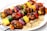 A plate of grilled skewers with chunks of meat, vibrant vegetables such as zucchini, yellow squash, red onion, and red and orange bell peppers. The skewers are arranged over a bed of cooked quinoa, showcasing a combination of charred marks and colorful, fresh ingredients.