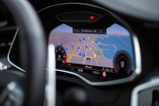 A close-up view of a car's digital dashboard displaying a navigation system. The map on the screen shows roads, parking symbols, and the temperature outside. The dashboard features sleek, modern design elements with a focus on functionality.