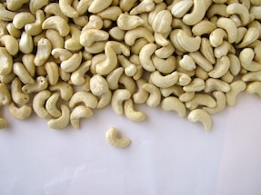 A large pile of shelled cashew nuts spread out on a plain, light-colored surface, with a few scattered away from the main group.