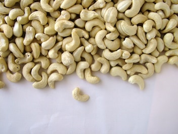 A large pile of shelled cashew nuts spread out on a plain, light-colored surface, with a few scattered away from the main group.