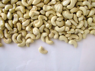 A close-up of golden cashews spilling gently from a navy-blue pouch against a warm wooden background.