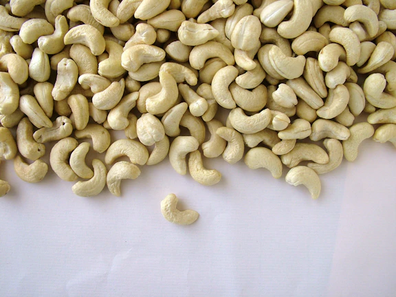 Close-up of natural cashew nuts spilling from a rustic burlap sack on a wooden table.