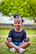 a little girl sitting in the grass with her hair in a bun