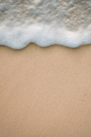 A close-up of a surf-inspired soap bar resting on a sandy beach with ocean waves in the background