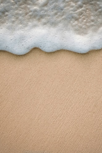 A close-up of a surf-inspired soap bar resting on a sandy beach with ocean waves in the background