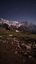A serene campsite set against the backdrop of snow-capped mountains under a starry night sky.