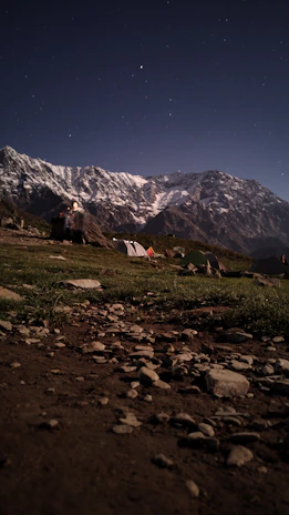A serene campsite at twilight with tents pitched under a star-filled sky near the mountain base.