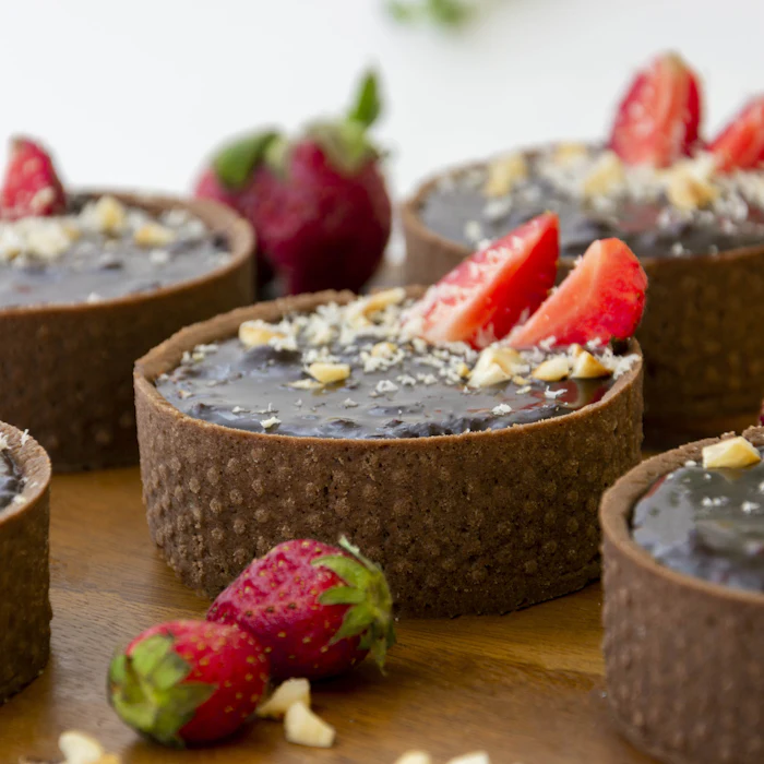 Schokoladen-Tartelettes mit frischen Erdbeeren auf dunklem Holztisch