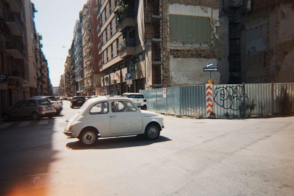 a small white car driving down a street next to tall buildings