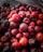 A close-up view of a collection of ripe, round berries with a textured surface, exhibiting varying shades of red and purple. The berries are densely packed together, highlighting their plump and juicy appearance.