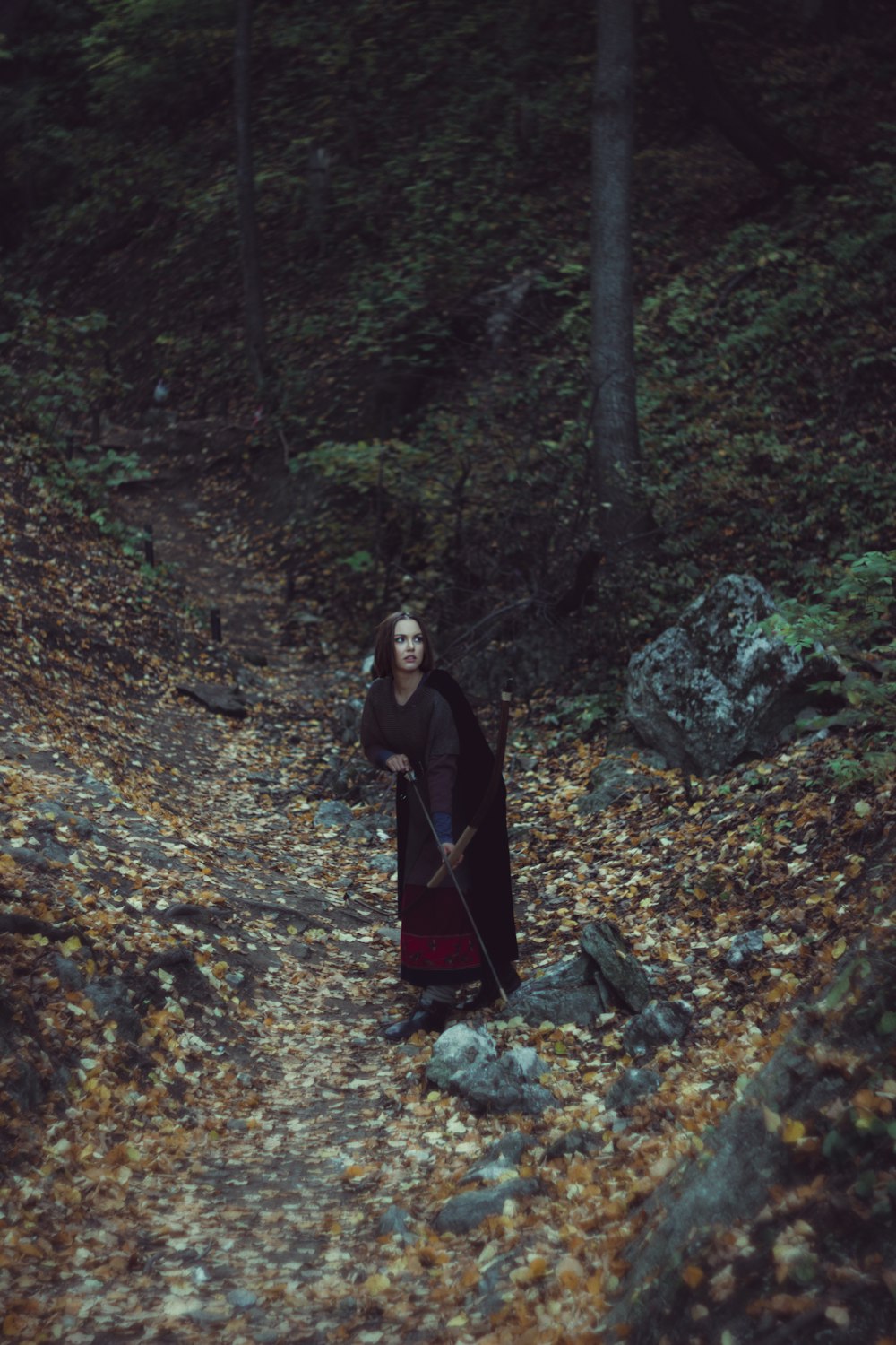 a woman in a black cloak is walking through the woods