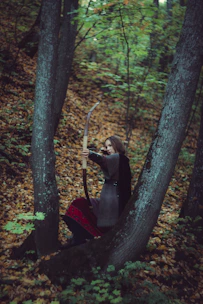 A focused participant drawing a bow in a sun-dappled forest clearing.