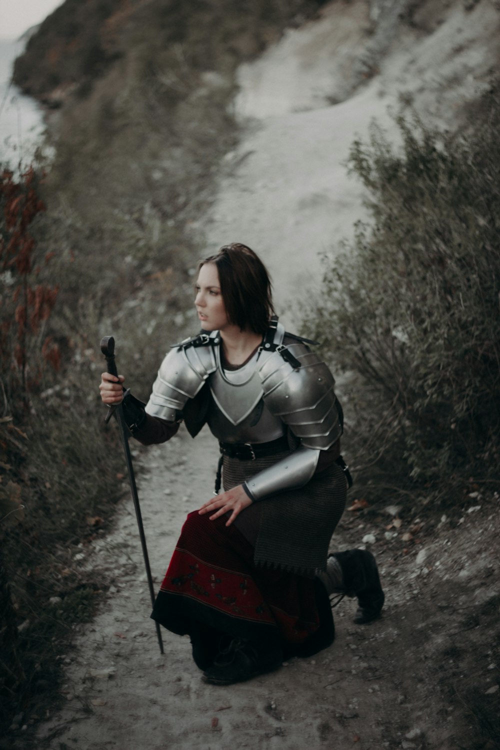 Une femme habillée en chevalier agenouillée sur un chemin
