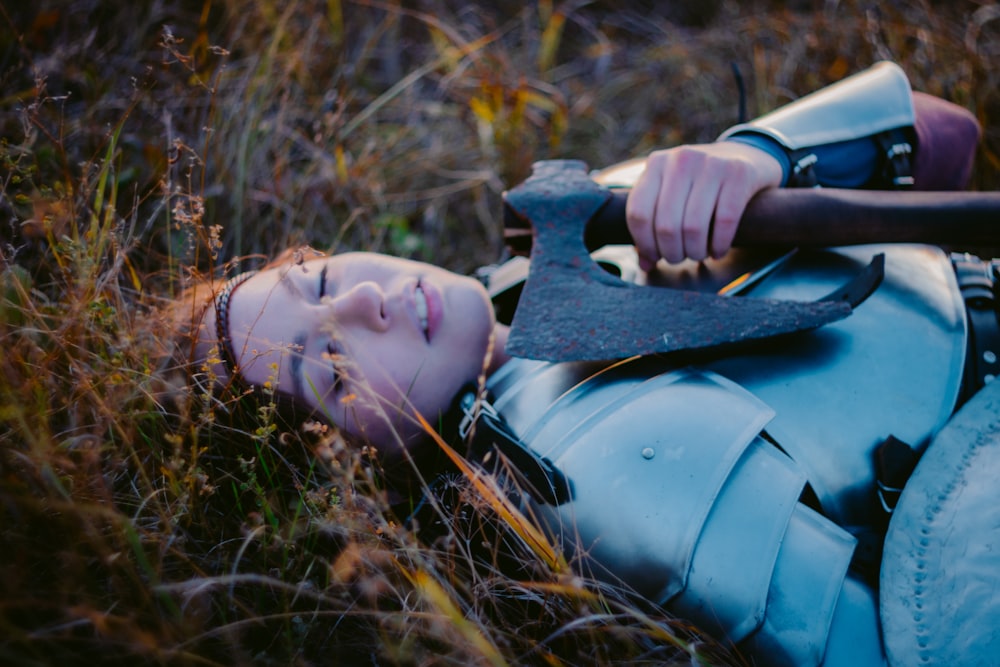 a woman laying in the grass with an axe in her hand