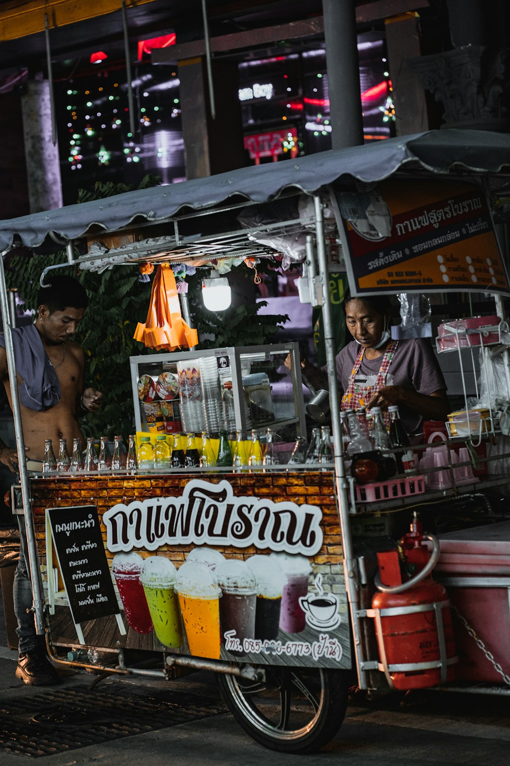 Un hombre parado detrás de un carrito de comida vendiendo bebidas