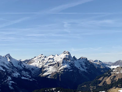 Snow-capped mountain peaks rising above lush green valleys under a clear blue sky.