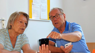 A friendly technician gently assisting an elderly woman with her smartphone in a cozy living room.
