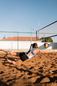 a woman dives to catch a ball on a beach