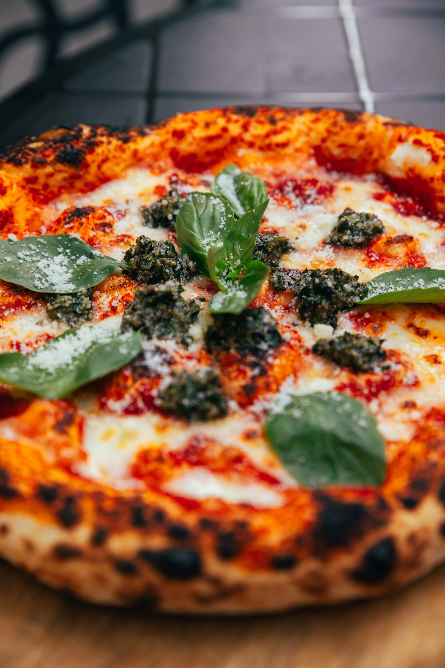 A wood-fired pizza with a leopard-spotted crust, melted fior di latte, dots of basil pesto and torn basil