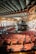 An opulent theater interior with ornate architectural details, featuring a grand, colorful ceiling adorned with intricate patterns and sculptures. Rows of plush red seats fill the space, leading down to a stage area. Large arched windows allow natural light to illuminate the richly decorated environment.