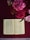 An open book lies on a richly textured maroon cloth, surrounded by a vibrant bouquet of pink and red flowers. The pages of the book display dense text in a clean, serif font. The scene is softly lit, highlighting the delicate details of the flowers and the intricate patterns of the cloth beneath.