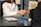 Two people sitting at a desk are shaking hands over paperwork, likely indicating the conclusion of a business deal or an agreement. One person is wearing a white shirt and the other is dressed in dark clothing. Other items present include a laptop, a small potted plant, and a clipboard with a pen.