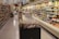 A grocery store aisle displaying various packaged foods on shelves. In the center, there is a promotional display of bags containing toffee popcorn, with a sign indicating the price. The aisle is well-lit, and the shelves are stocked with an assortment of products, including snacks, dairy, and bread.