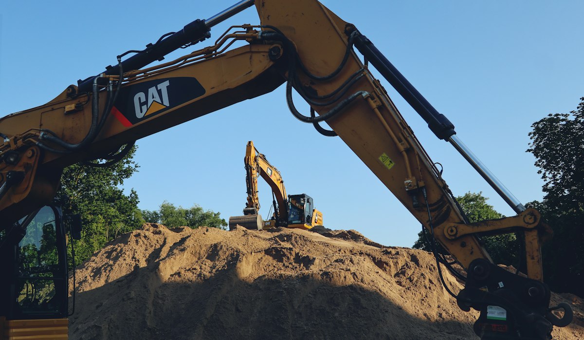 Excavators and a raised boom over exposed earth at a sitework area.