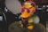 A cartoonish duck figure with bright yellow body, wearing oversized pink glasses and blue earmuffs with a colorful hat labeled 'Duck DJ'. It stands on top of a drum in a music-themed setting with other drum parts visible in the background.
