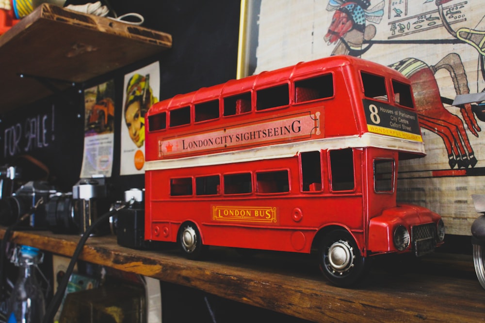 a red double decker bus sitting on top of a wooden shelf