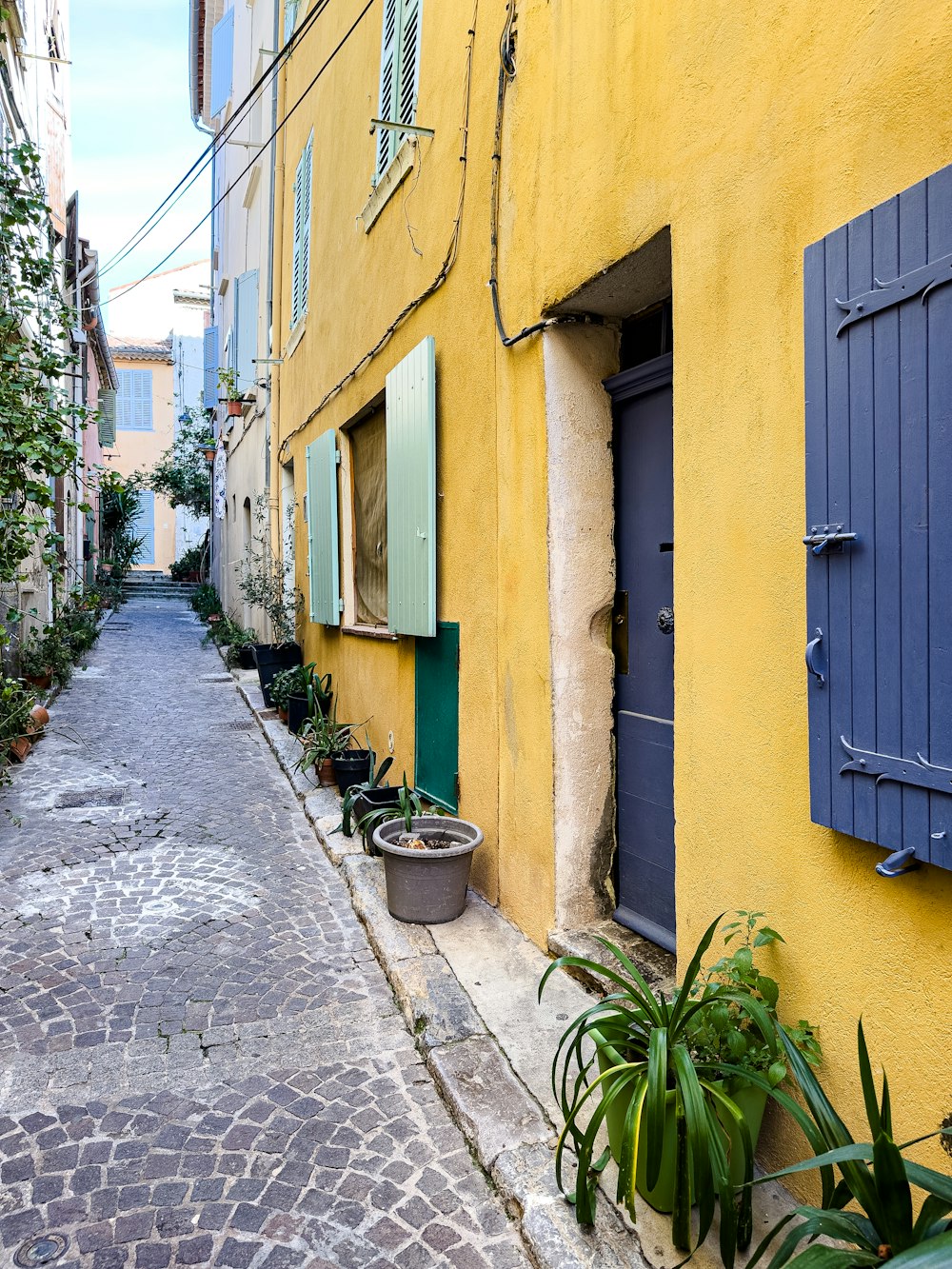 Una calle estrecha con un edificio amarillo y persianas azules