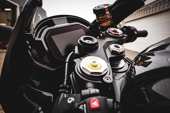 The close-up view captures the dashboard and controls of a motorcycle, showcasing various knobs, dials, and a digital display. The intricate details of the handlebar and control mechanisms are visible, highlighting the craftsmanship and design of the vehicle. The background is slightly out of focus, emphasizing the motorcycle's features.