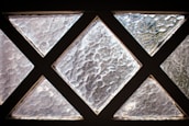 A series of textured glass panes arranged in a grid with triangular shapes, creating a pattern that allows diffused light to pass through. The glass has a rough, wavy surface that distorts the view.