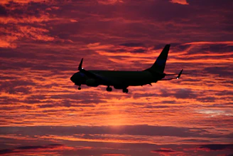 A breathtaking high-resolution photo capturing a vibrant sunset sky with a silhouette of a soaring airplane.
